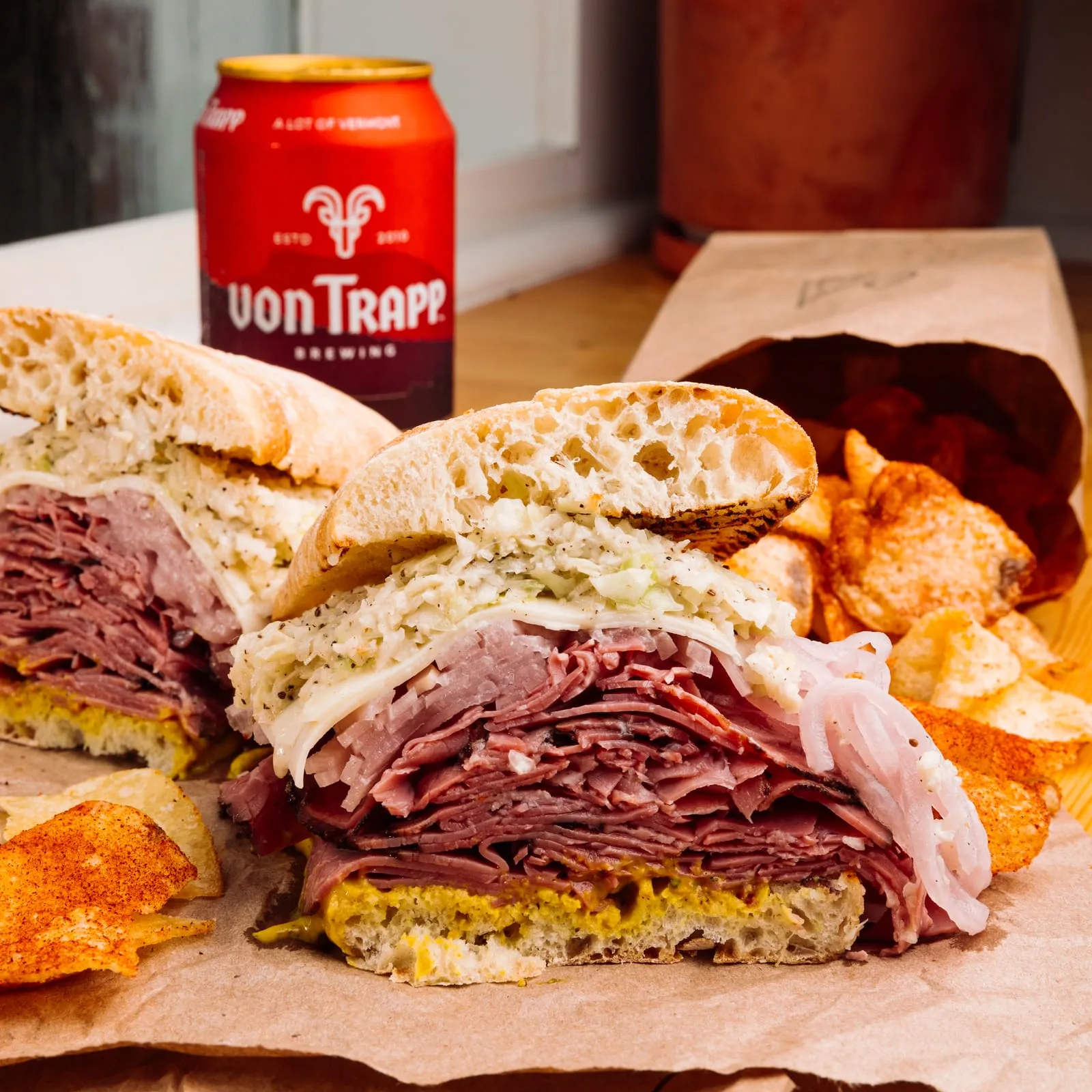 A stacked pastrami sandwich with chips and a cold can