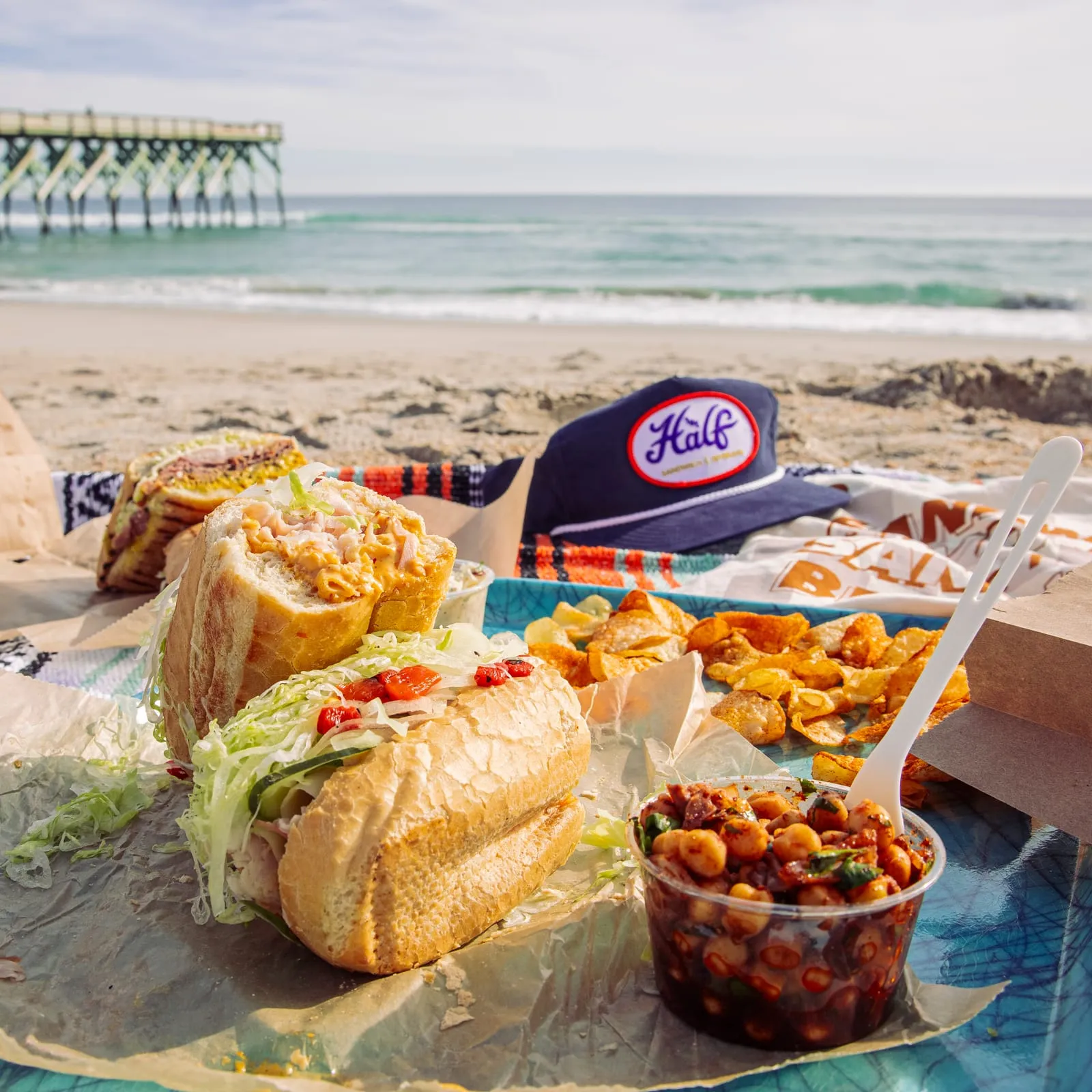 Sandwiches, chips and a Half cap on a beach blanket