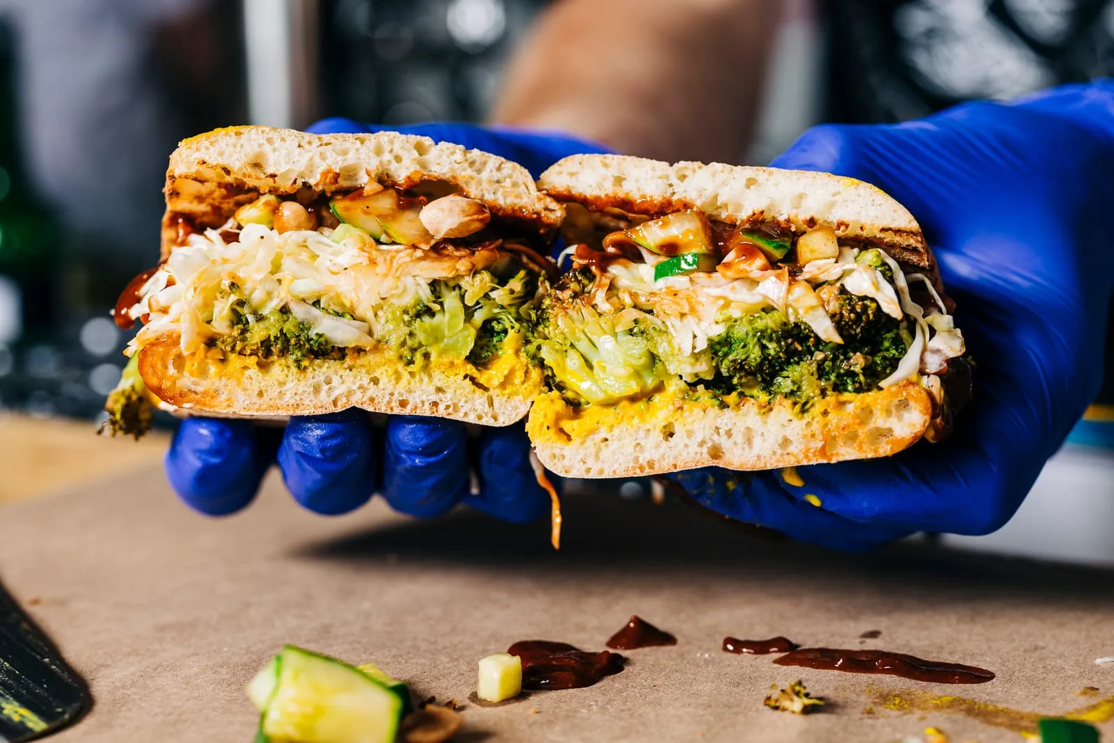 Gloved hands holding a broccoli sandwich cut in half