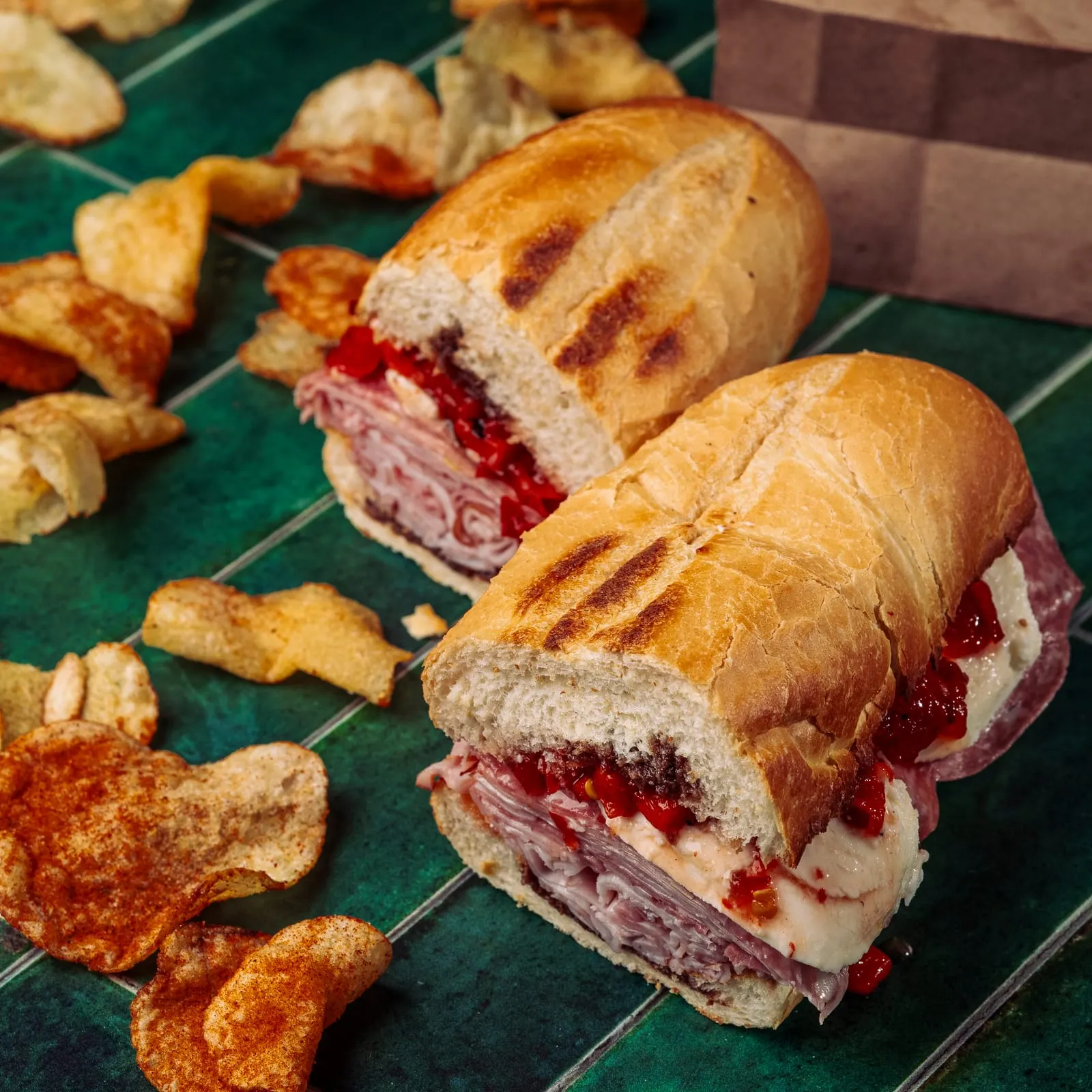 Sandwich halves and chips on a green tiled table