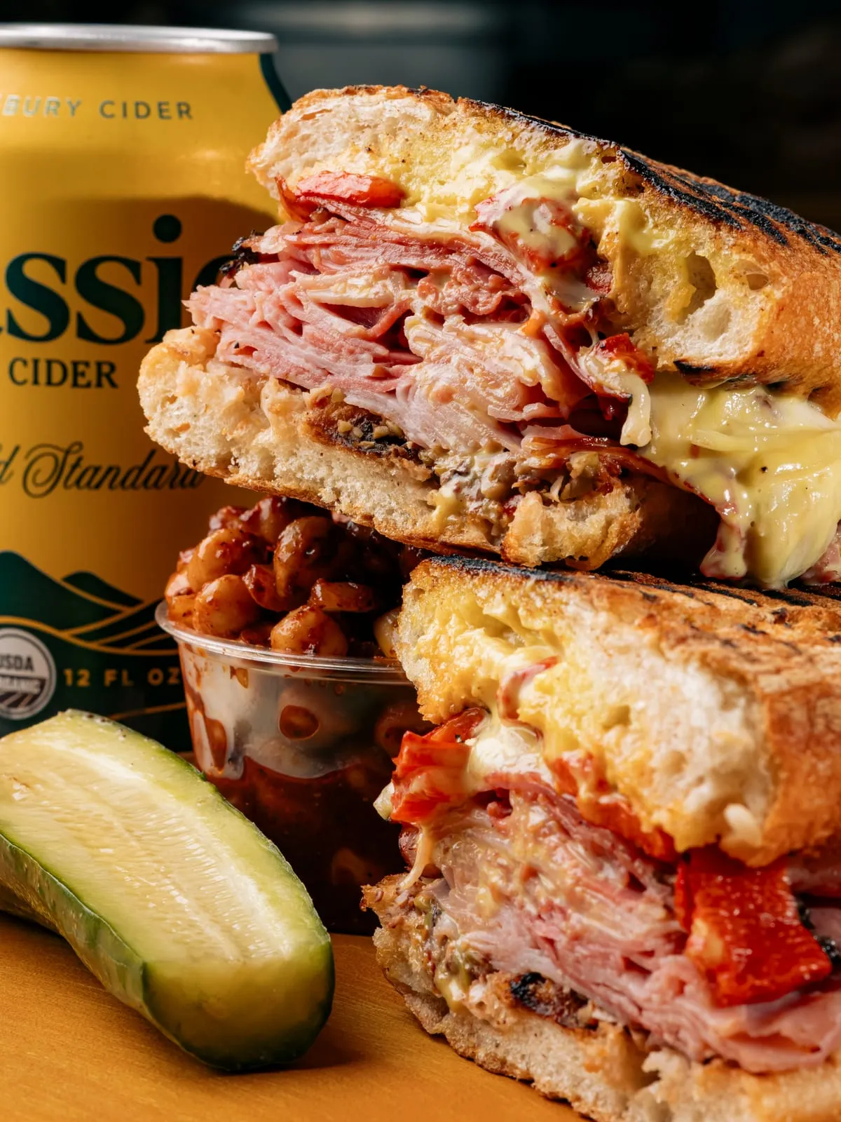 A sandwich with a cider can, chips and a pickle