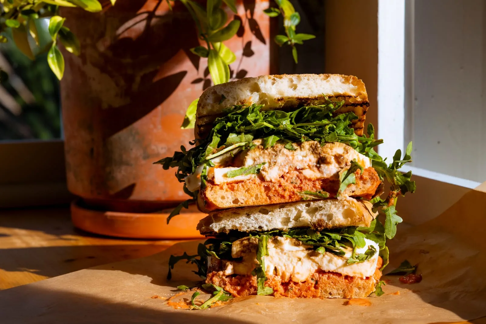 A sandwich cut in half, stacked and full of greens